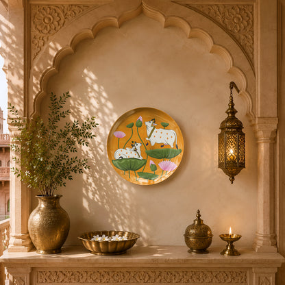 Luxury ceramic wall plate inspired by Pichwai art with graceful cows, lotus blooms and vibrant saffron tones.
