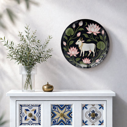 Vaastu ceramic wall plate featuring a white cow surrounded by pink lotus flowers and green leaves