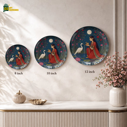 Glossy ceramic wall plate featuring a woman in a red sari surrounded by flowers and white cranes against a deep blue sky.